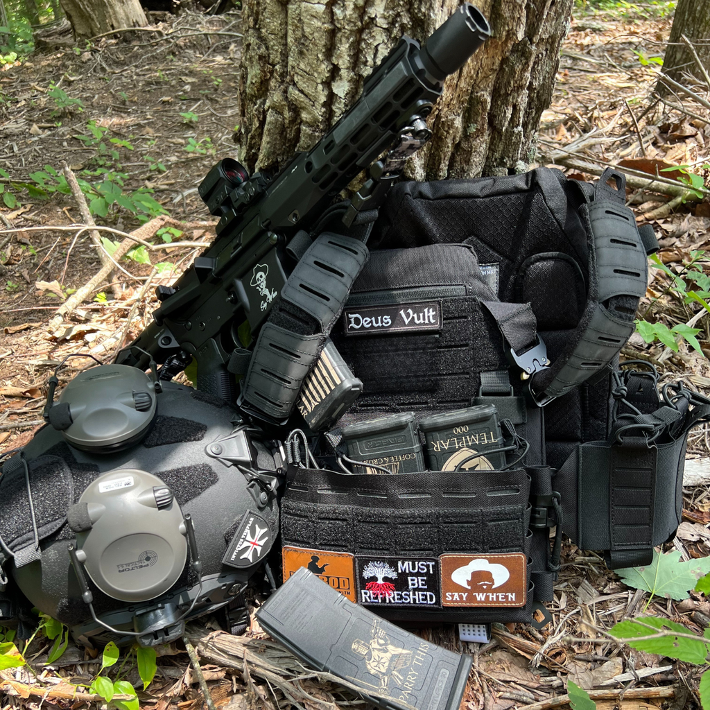Invictus Pattern MK I Modular Plate Carrier setup with accessories and tactical gear in a forest.